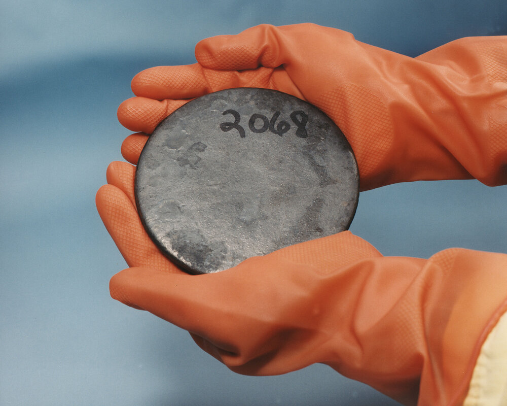 Próbka wysoko wzbogaconego uranu metalicznego oznaczona numerem. Numer widoczny na powierzchni jest tylko fizycznym oznaczeniem obiektu: jego znaczenie musi wynikać z kontrolowanego rejestru, a zawartość U-235 z identyfikowalnej dokumentacji i właściwego pomiaru izotopowego. Same wygląd i oznaczenie nie potwierdzają tożsamości materiału. Zdjęcie: U.S. Department of Energy.